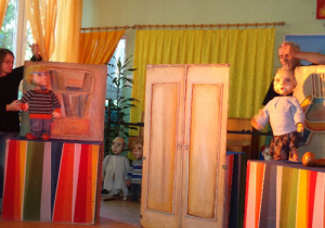 Po lewej stronie animatorka trzyma marionetkę chłopca, po prawej marionetkę starszej kobiety